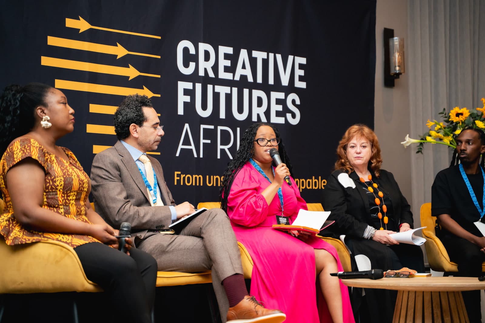 three women and two men sit on stage in a panel discussion in front of a navy blue backdrop at Creative Futures Africa